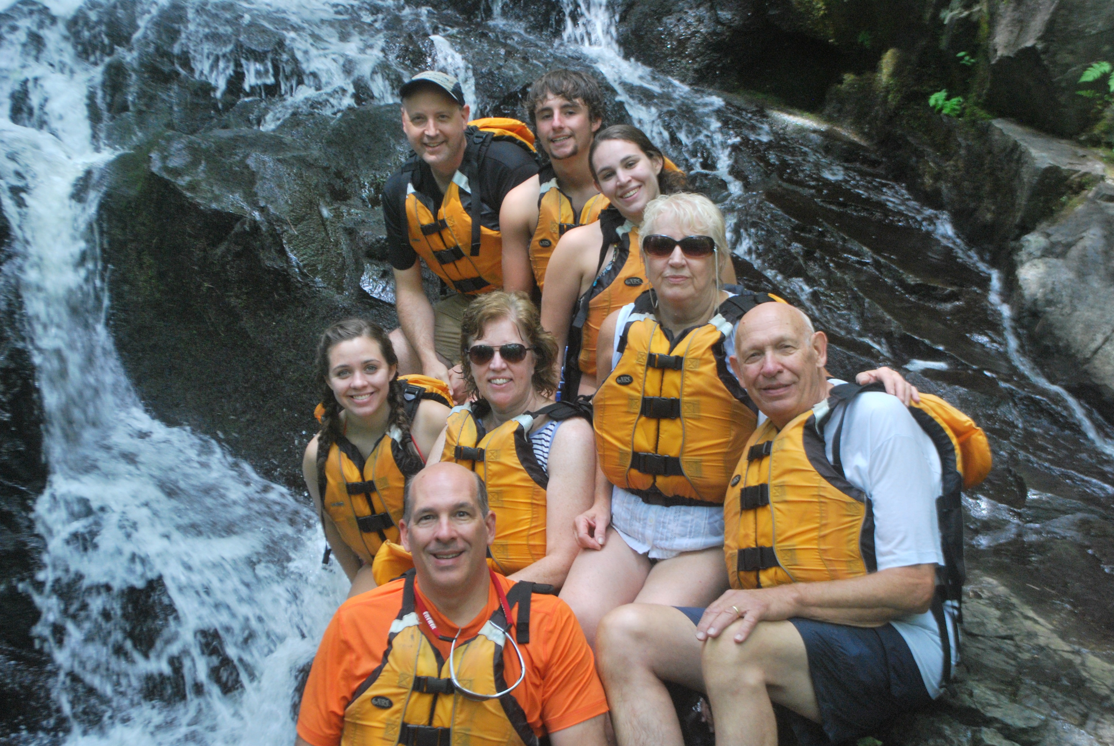 group of people with life vests posing as they smile in front of a waterfall