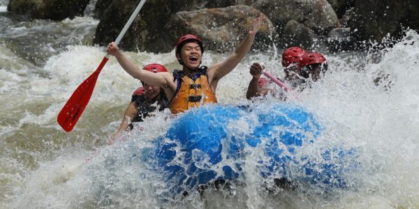 man with his arms in the air as water splashes on him and a group of rafters