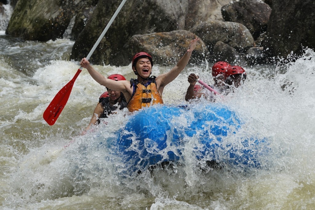 man with his arms in the air as water splashes on him and a group of rafters