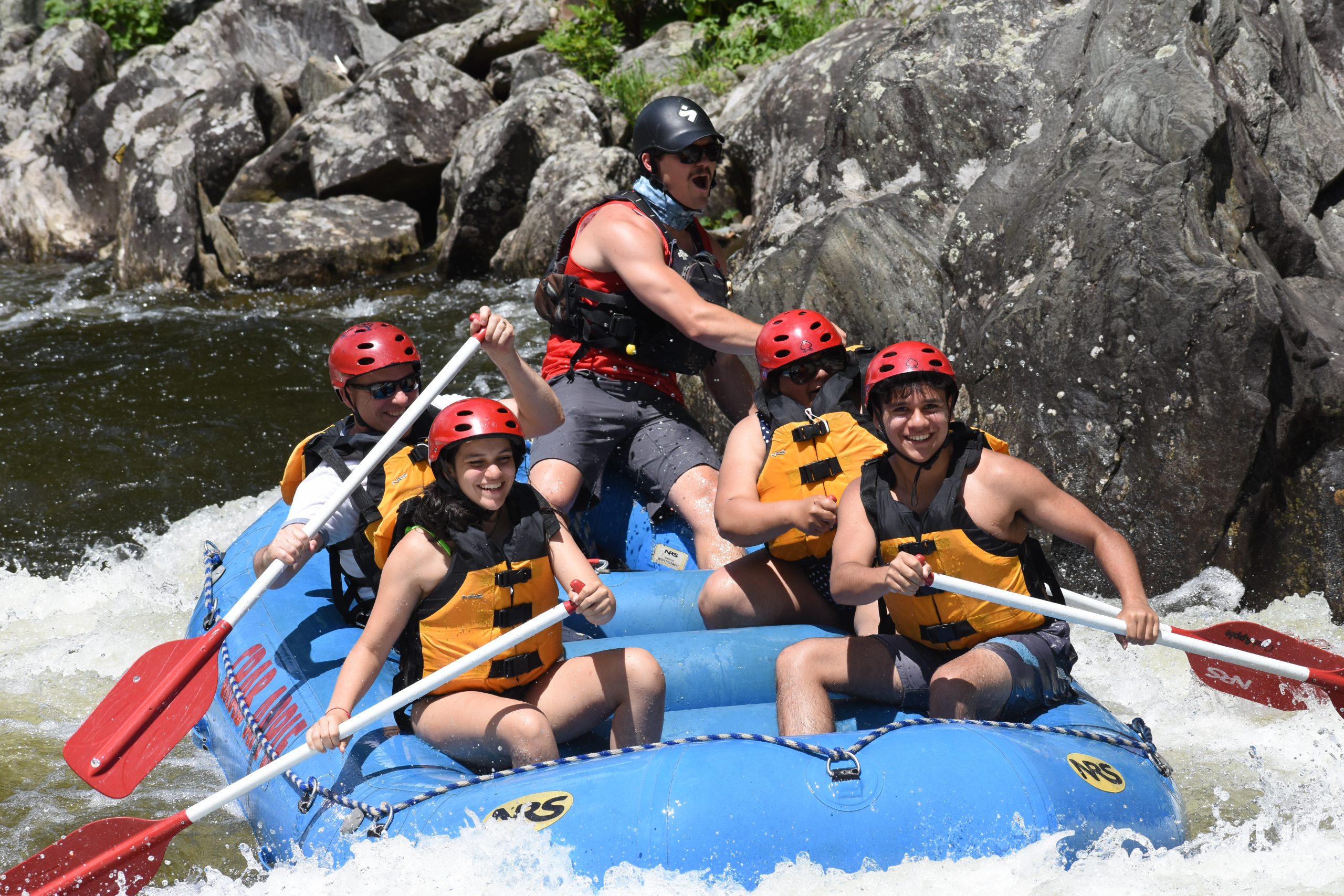 group of rafters paddling as the man in the back has his mouth his open